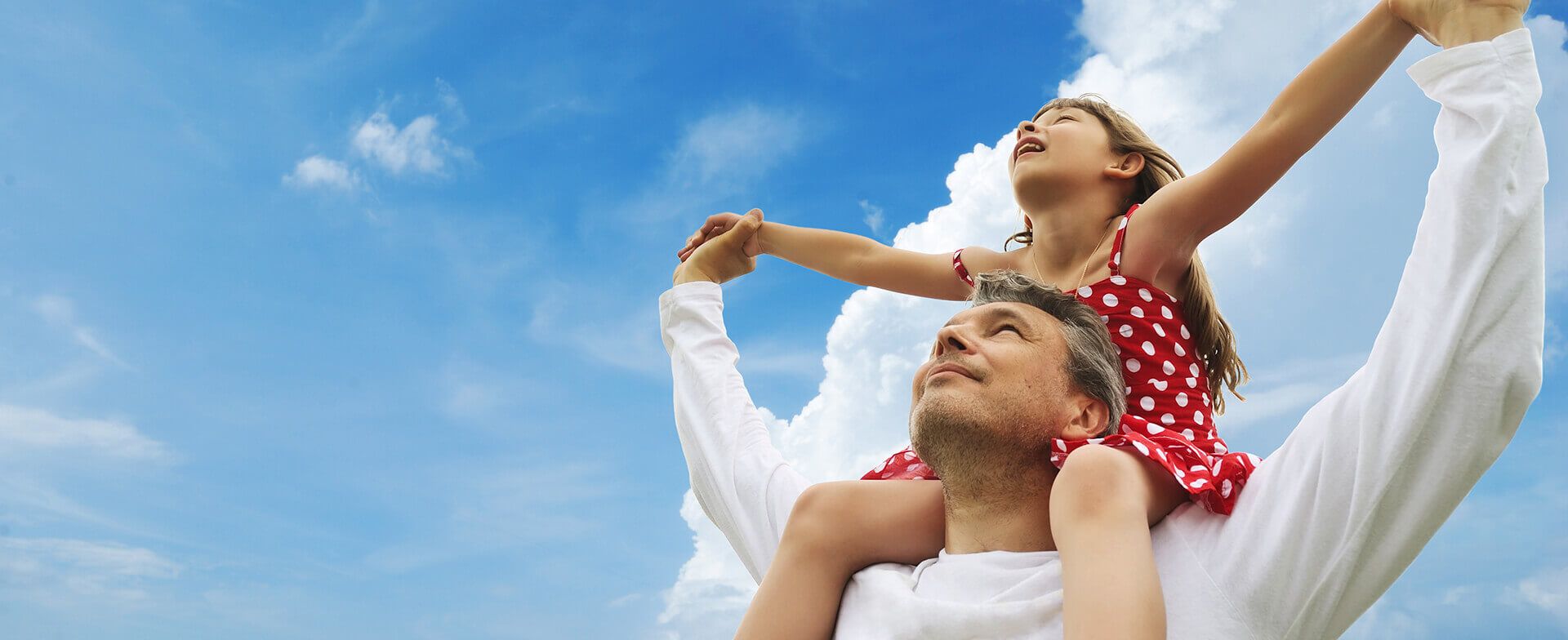 Dad lifting his daughter on his shoulders and looking up to the sky