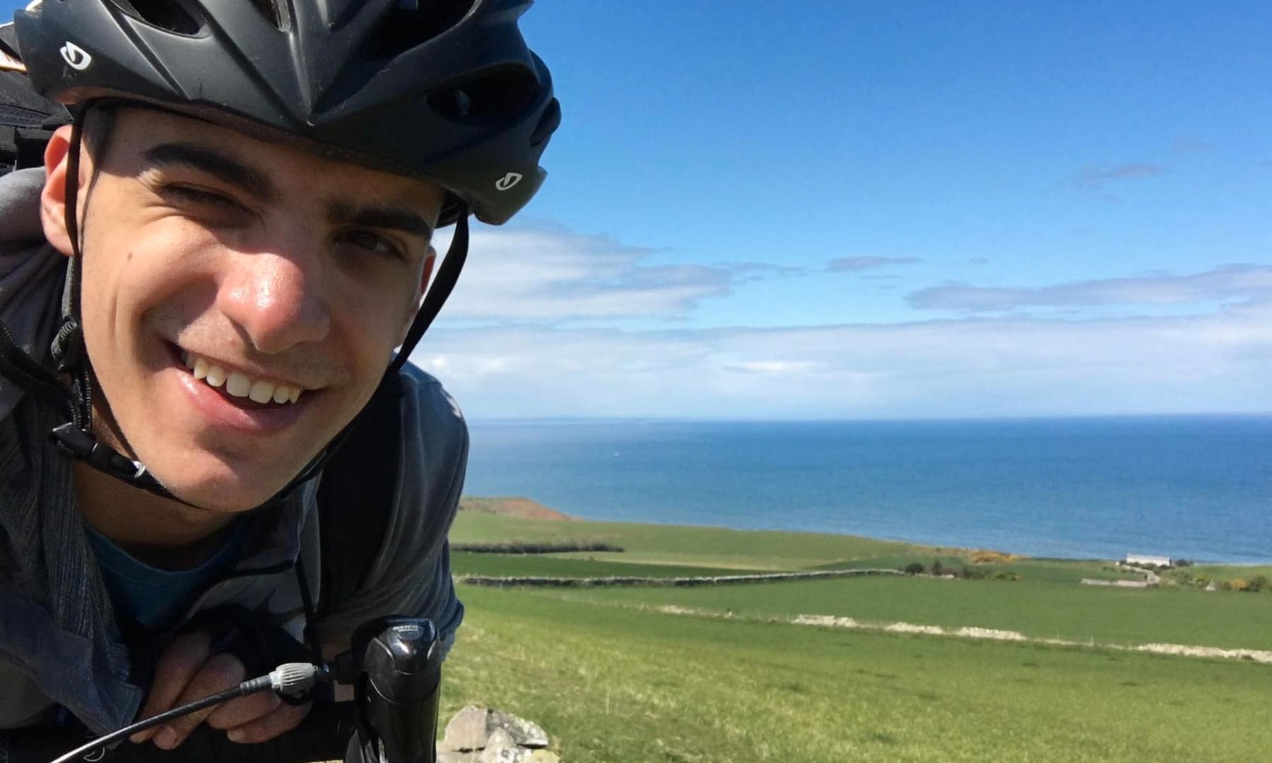 Kleon taking a selfie while on his bike with pastures and sea behind him